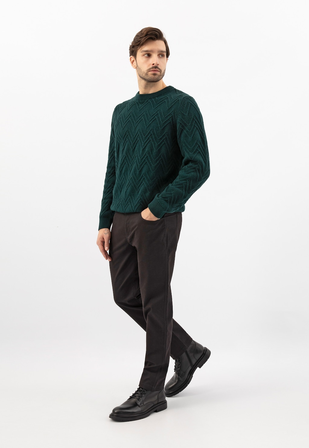Model w zielonym swetrze z wzorem w zygzaki i ciemnych spodniach prezentuje czarne klasyczne bikery Wojas model 24106-51 ze skóry licowej, idealne do eleganckiej stylizacji.