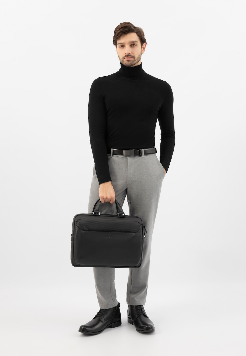 Elegancka czarna torba Wojas model 90024-81 z przegrodą na laptopa prezentowana w biznesowej stylizacji z czarnym golfem i szarymi spodniami.