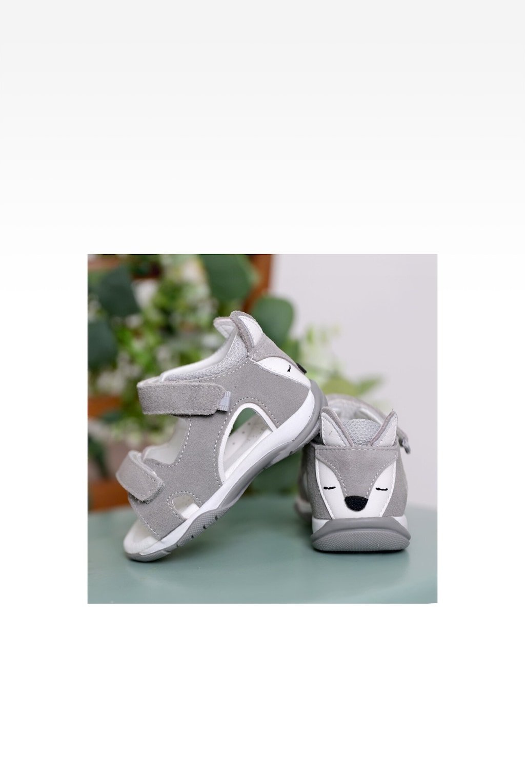 Szare sandały dziecięce Bartek 84411-80 z uroczą aplikacją wilka na pięcie, widok z boku, na zielonym podłożu z roślinami w tle.