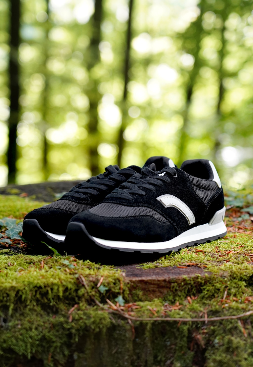 Czarne sportowe sneakersy RELAKS R34202-89 z srebrnym logo, zamszowa cholewka, biała podeszwa, ustawione na omszałym kamieniu w lesie.