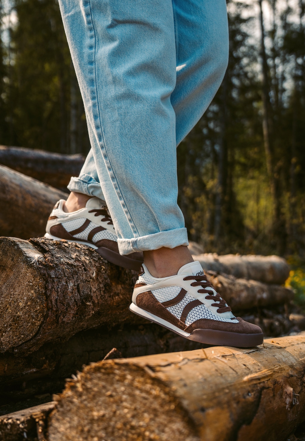 Damskie sneakersy RELAKS R46185-82 beżowo-brązowe retro z ażurową cholewką, noszone z jeansami podczas spaceru po lesie na pniach drzew.