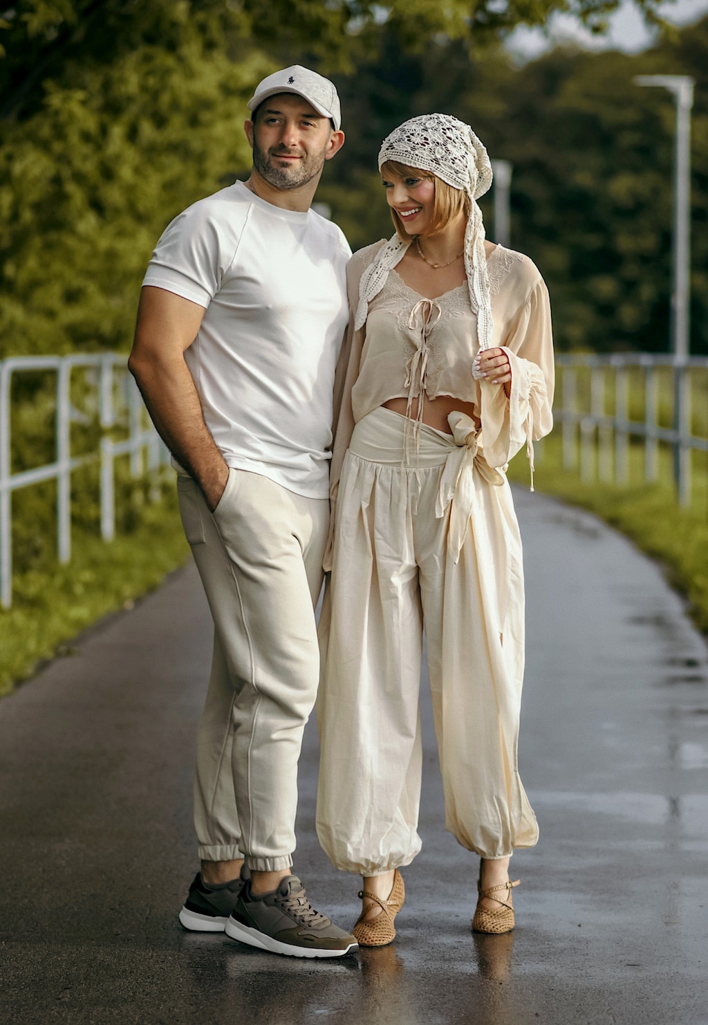 Brązowe plecione baleriny RELAKS z krzyżującymi się paskami na stopie kobiety, na tle pary stojącej na ścieżce na zewnątrz.