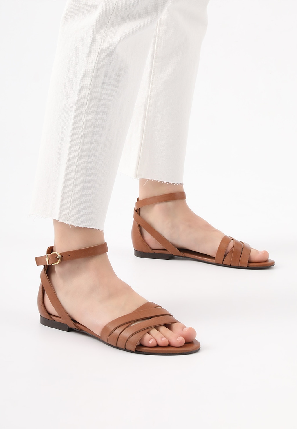 Brązowe sandały damskie Wojas model 76015-53 w stylu urban, płaskie z paskiem na kostce, noszone do białych spodni, widok z boku.