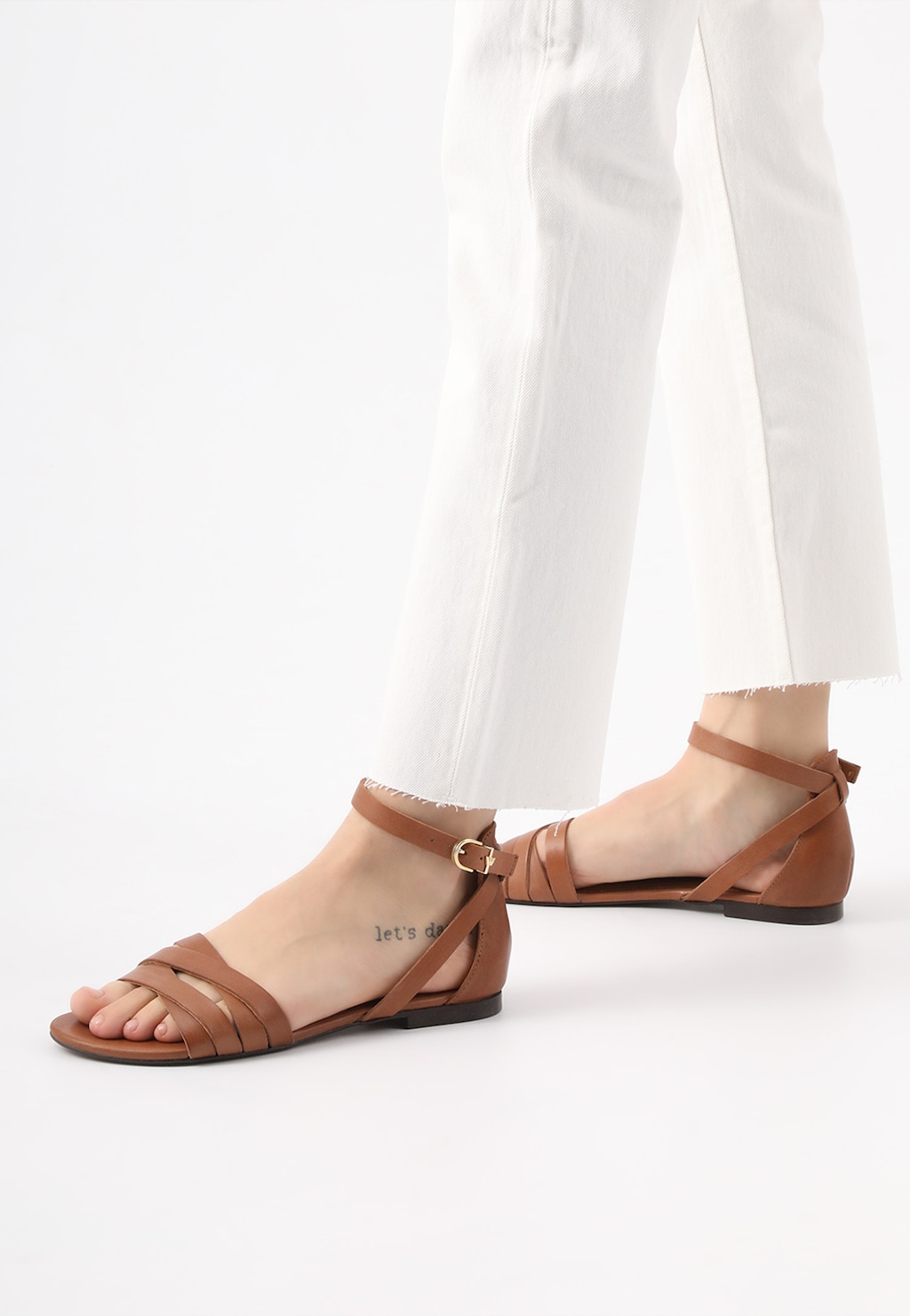 Brązowe sandały damskie Wojas model 76015-53 w stylu urban prezentowane na nodze modelki w białych spodniach, ukazujące elegancką formę i paski z klamrą.