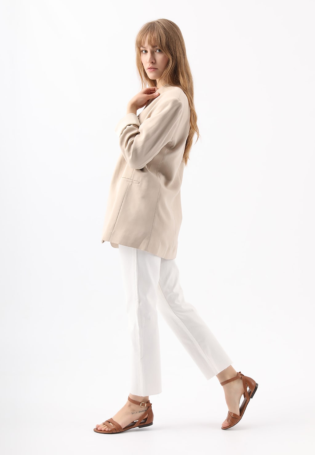 Elegancka kobieta w beżowej marynarce i białych spodniach, prezentująca brązowe sandały damskie Wojas model 76015-53 w stylu urban, widok z boku.