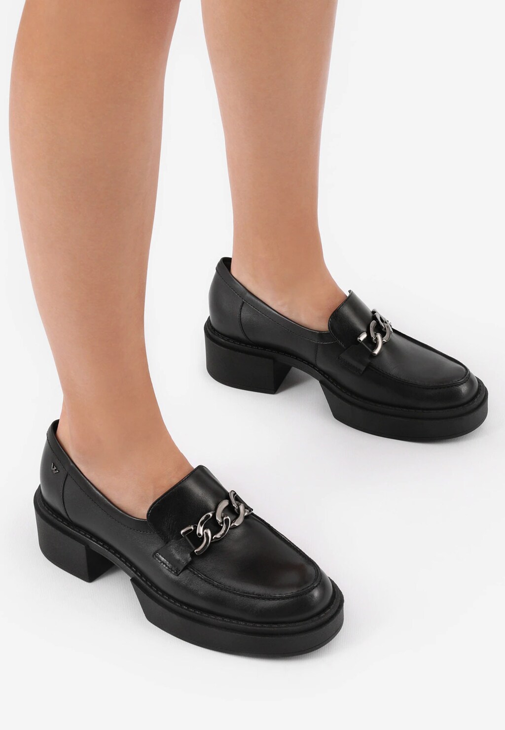 Czarne mokasyny damskie Wojas 46113-51 w stylu urban z metalowym łańcuszkiem na przodzie, na stabilnym niskim obcasie, prezentowane na nogach modelki.