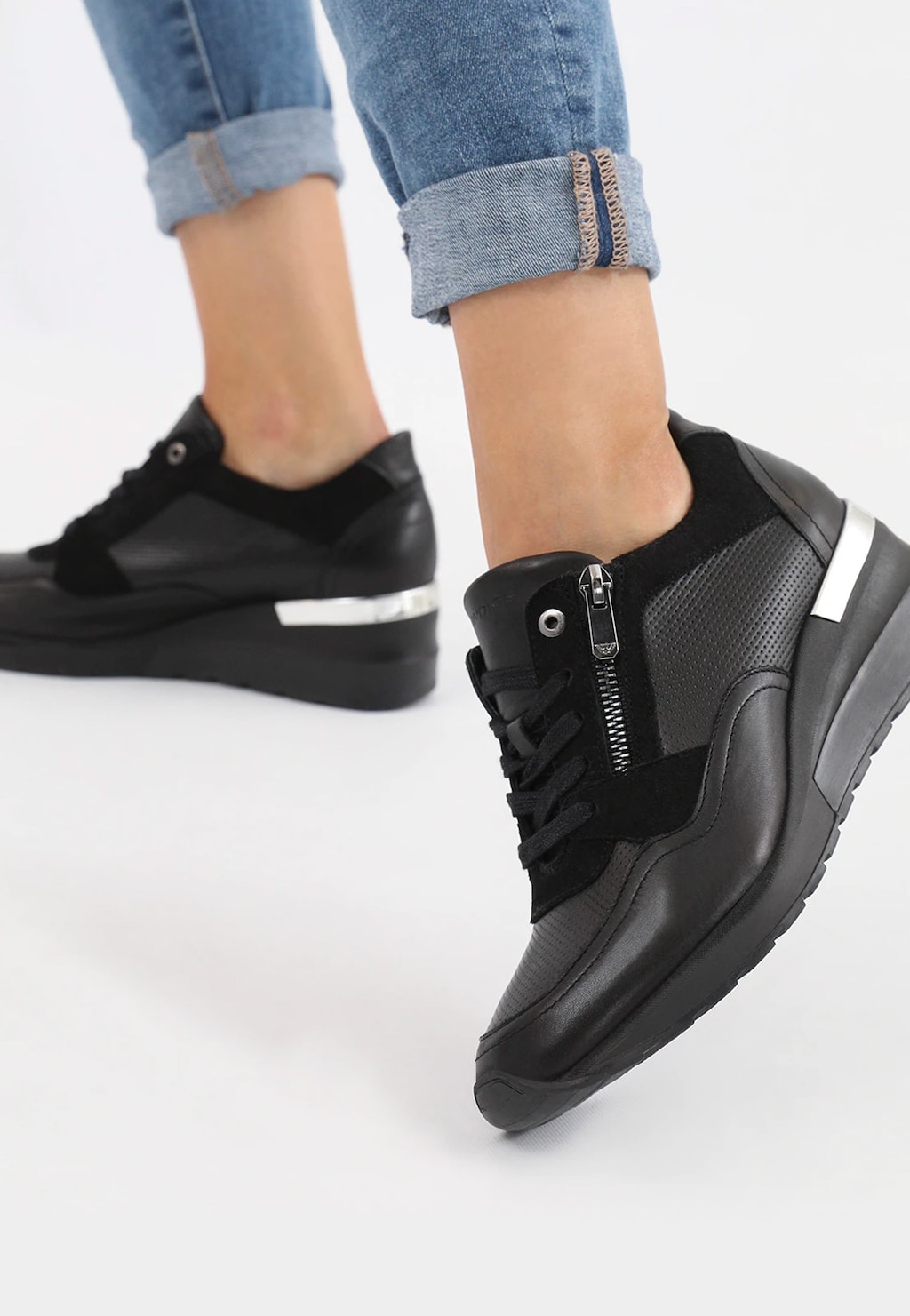 Czarne sneakersy damskie Wojas 46091-71 z ozdobnym zamkiem, noszone z podwiniętymi jeansami. Buty mają białe elementy i sportowy design na koturnie.