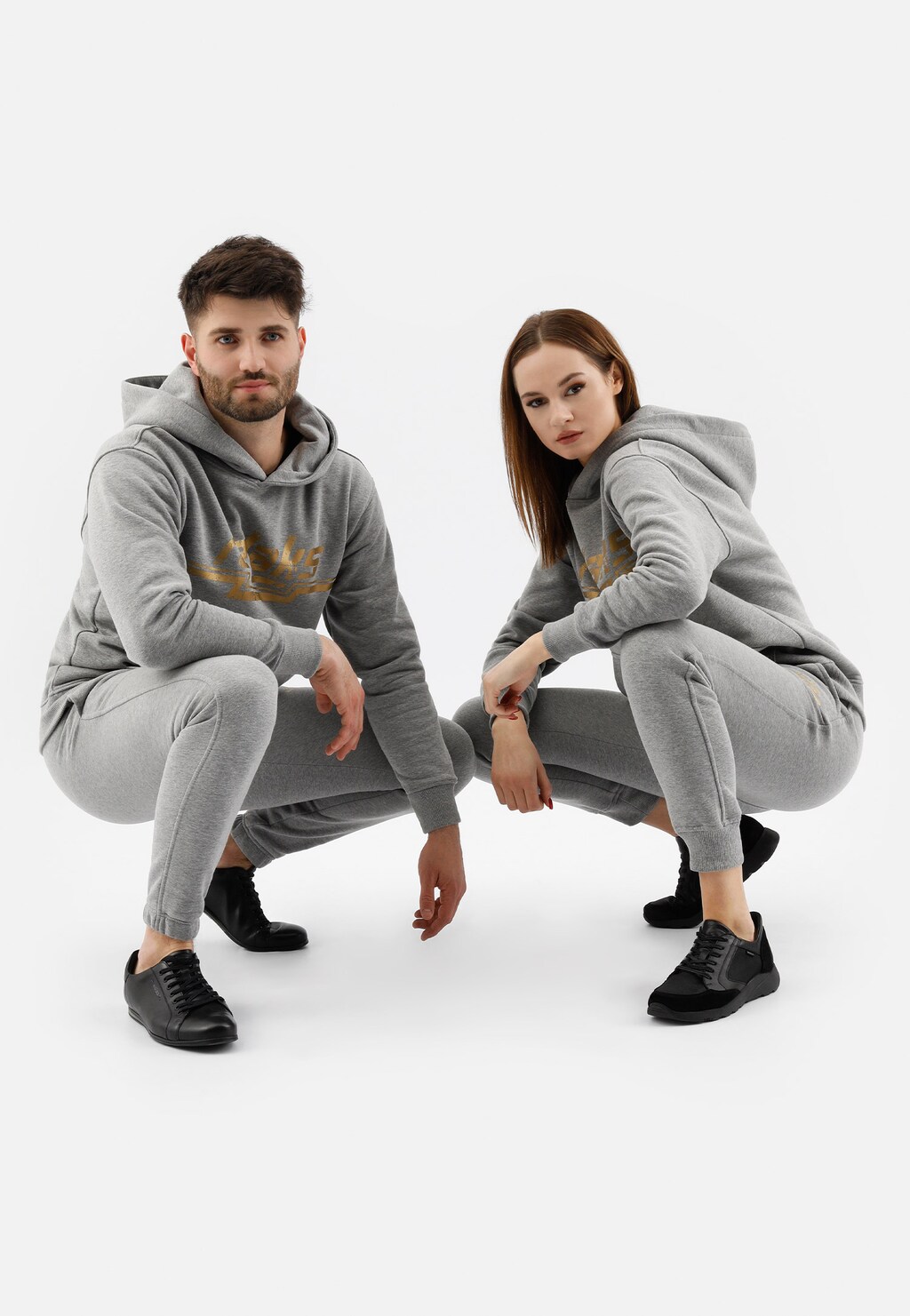 Popielate spodnie dresowe damskie bawełniane model 98024-80 prezentowane przez kucających modeli w komplecie z dopasowanymi bluzami z kapturem i butami marki Relaks.